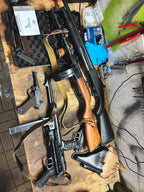 Two rifles on a wooden table with various tools and equipment around.