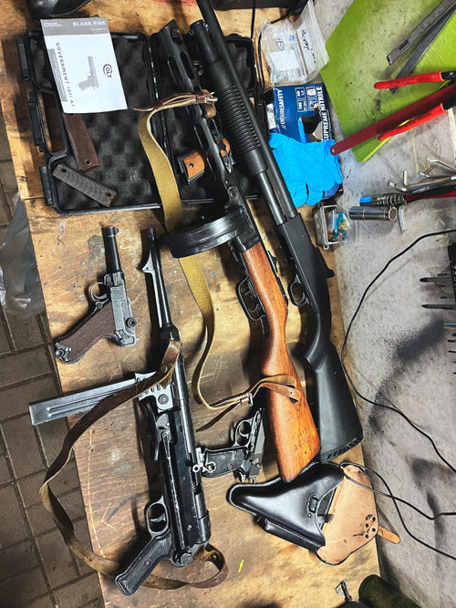 Two rifles on a wooden table with various tools and equipment around.