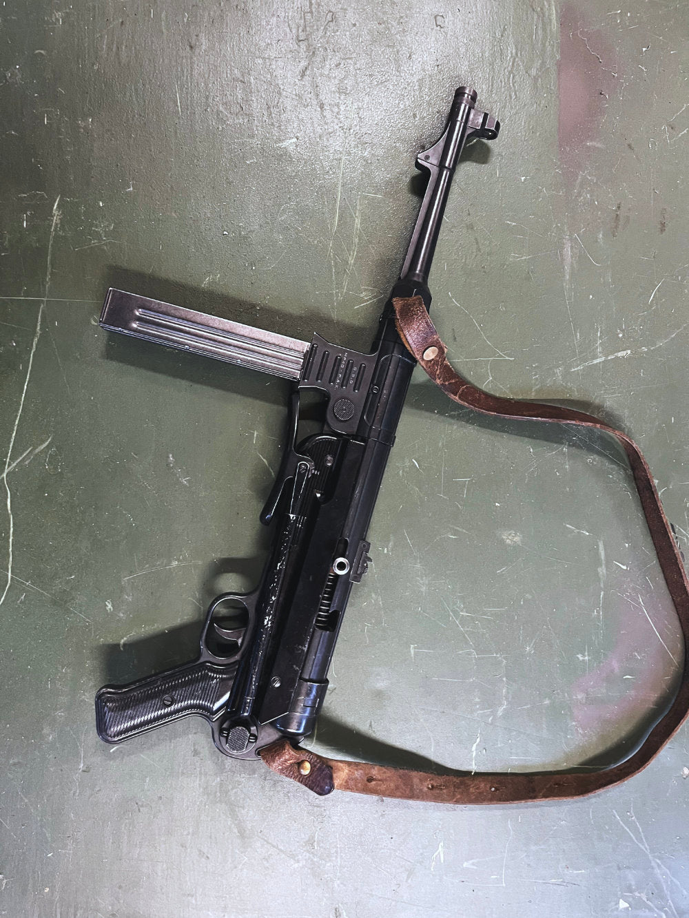 Black firearm with leather strap on a green surface