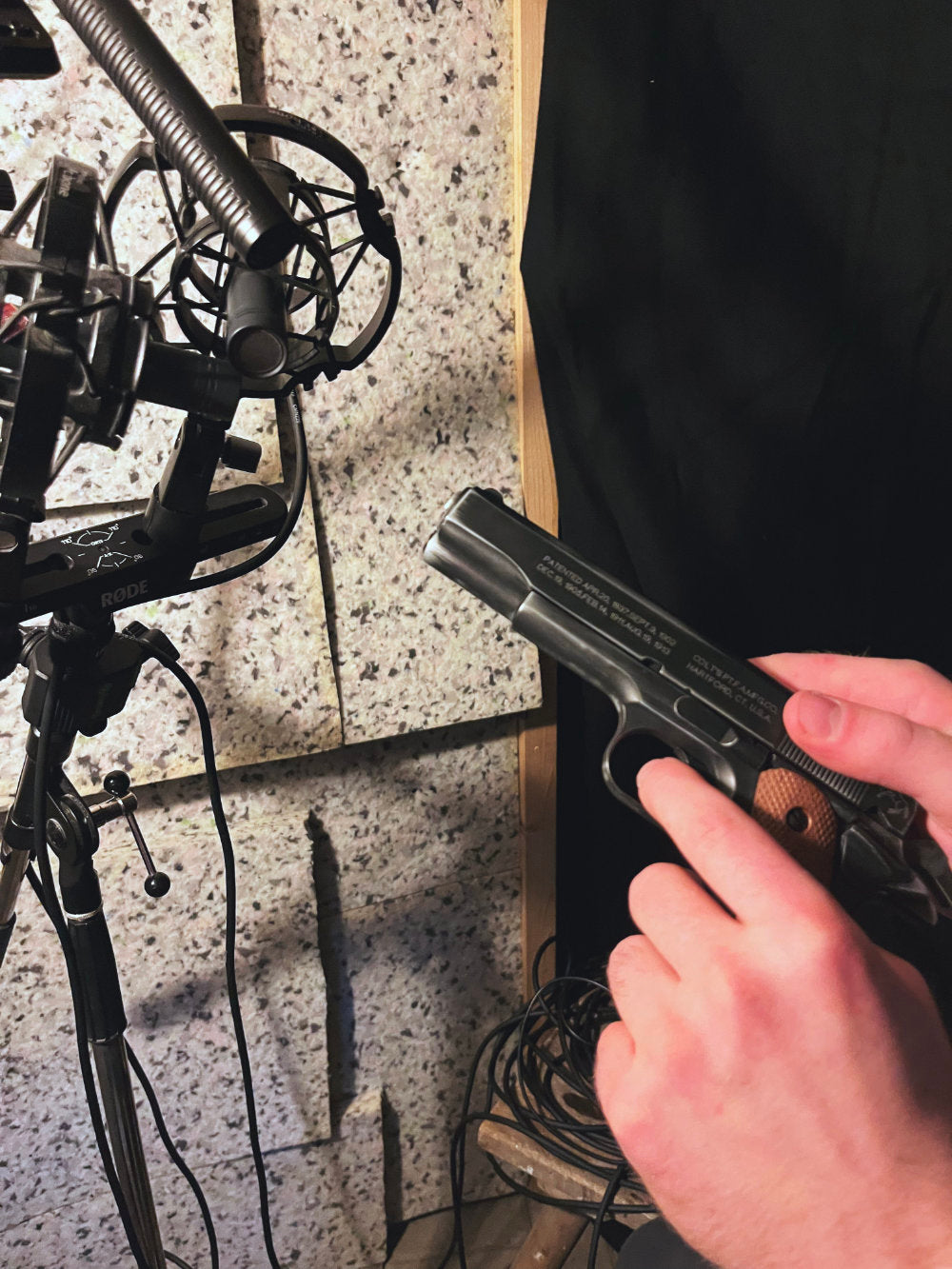 Hand holding a handgun near a microphone stand on a speckled surface