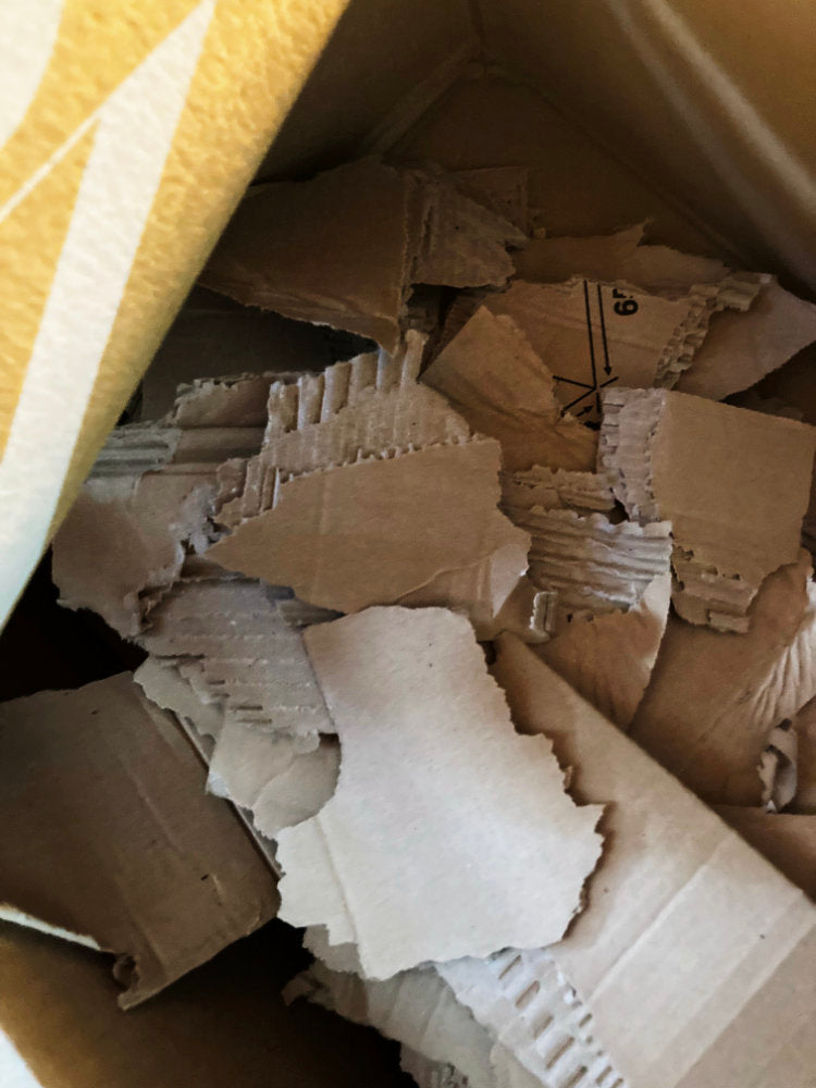 Pile of crumpled cardboard pieces inside a yellow trash bin.