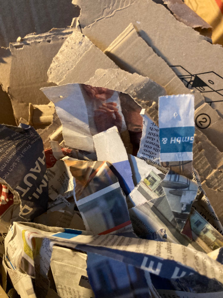 Pile of crumpled newspaper and paper bags with visible text and logos.