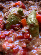 Close-up of a chili dish with beans, tomatoes, and peppers.