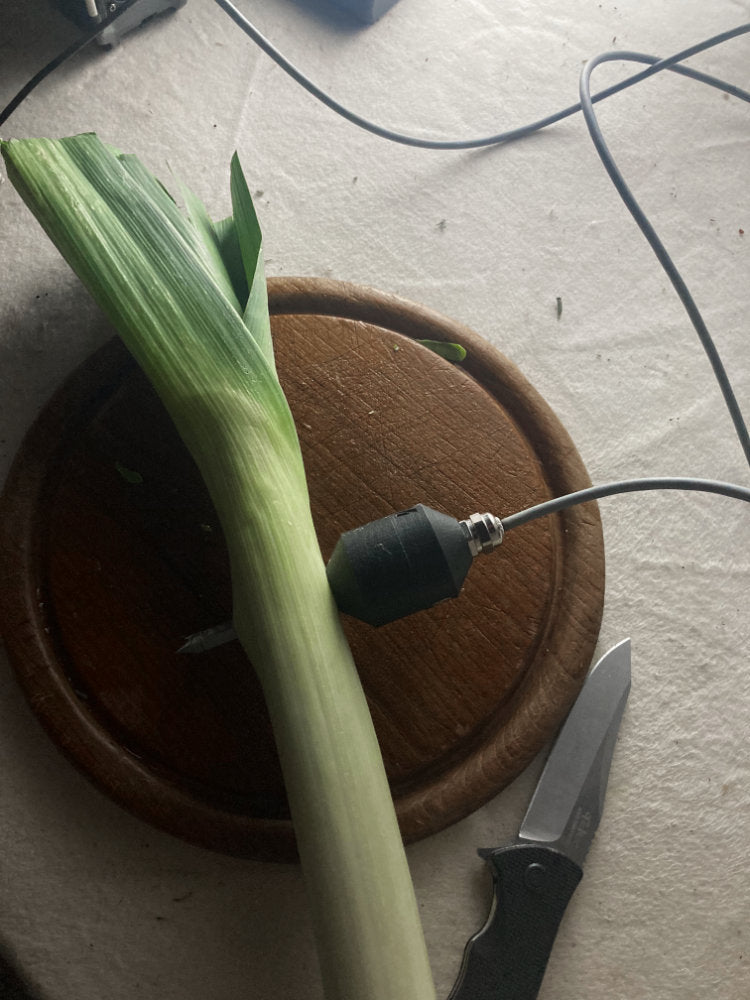 Long green leafy vegetable on a wooden board with a knife and black cable in the background.